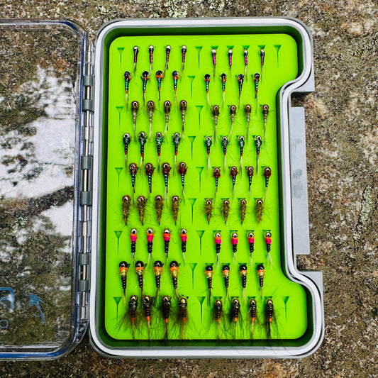 The Depth Charge Fly Box by Fly Life Outdoors laying on a rock by the river, showing an open overhead shot.