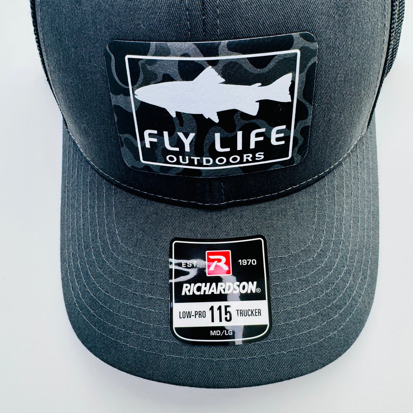 Close up view of the patch and bill of The FLO 115 Trucker in Charcoal with White Trout/Black Skies Camo patch | Charcoal/Black