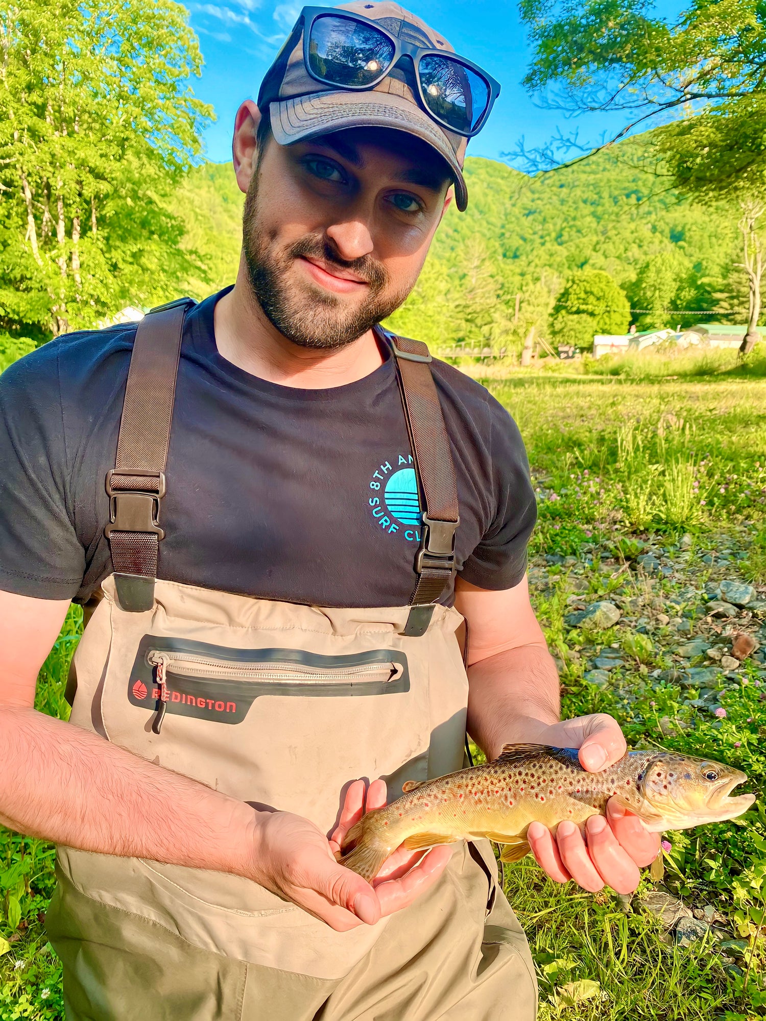 Fly fisherman proudly holding a small brown trout in a sunny mountain stream | Fly Life Outdoors