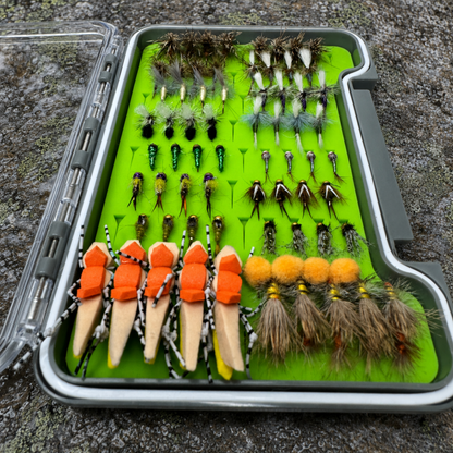 All-Water Arsenal loaded fly box angled view on granite river rock displaying 70 hand-tied dry flies, nymphs, and stonefly patterns for North Carolina trout fishing