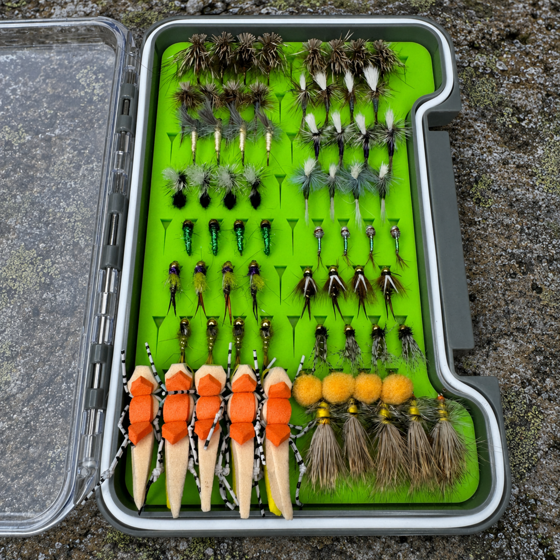 All-Water Arsenal loaded fly box on river rock with full trout fly assortment including dry flies, Pheasant Tails, Copper Johns, and foam hopper patterns for NC Hatchery Supported and Delayed Harvest streams
