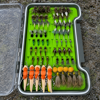 All-Water Arsenal loaded fly box on river rock with full trout fly assortment including dry flies, Pheasant Tails, Copper Johns, and foam hopper patterns for NC Hatchery Supported and Delayed Harvest streams