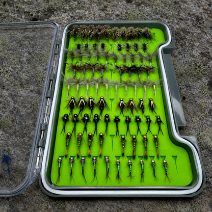 Essentials loaded fly box open on river rock displaying 82 hand-tied trout flies organized by pattern from dry flies to tungsten nymphs and midges for North Carolina trout fishing