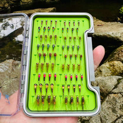 The Depth Charge Fly Box by Fly Life Outdoors in someone's hand by the river with a rock in the background.