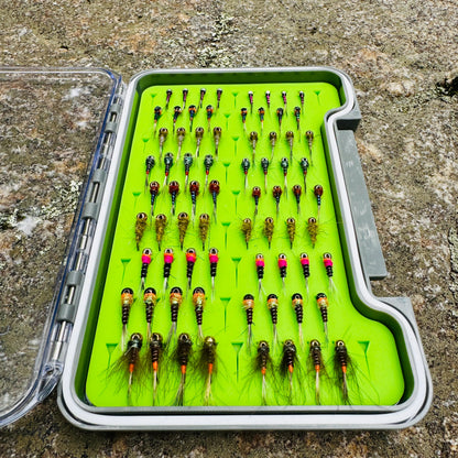Depth Charge Fly Box open on granite rock, loaded with rows of beadhead nymphs in gold, copper, green, and pink bead patterns on green foam insert