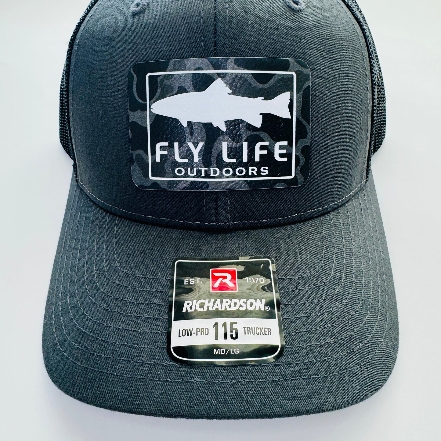 Patch and bill close up view of The FLO 115 Trucker in Charcoal with White Trout/Black Skies Camo patch | Charcoal/Black
