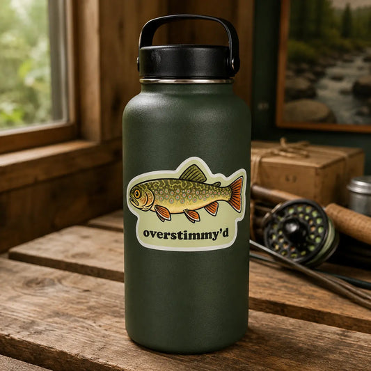 Overstimmy’d brook trout sticker on a green water bottle beside a fly rod and reel